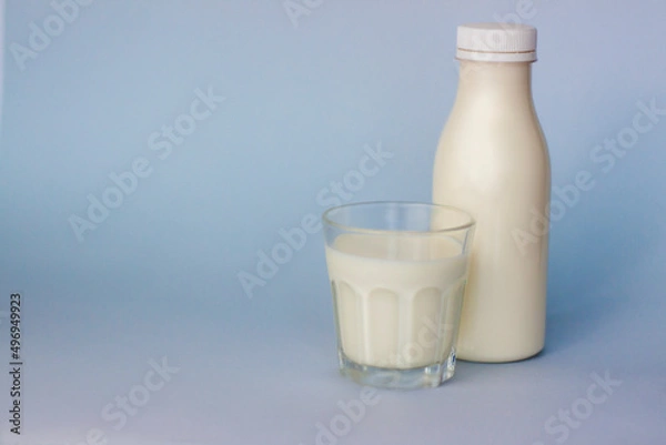 Fototapeta A glass and a bottle of white milk, highlighted on a blue background, close-up.
