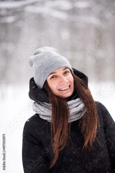 Obraz Portrait of a beautiful young smiling girl in a snowy winter in a gray hat and black jacket