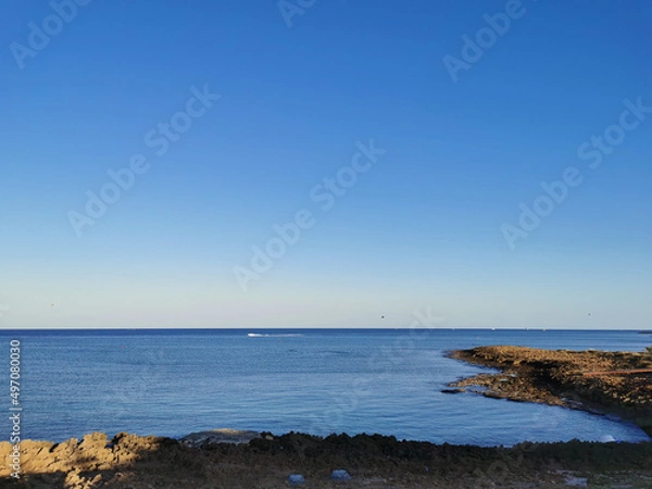 Obraz The rocky coast of the Mediterranean Sea from long-hardened lava, waves against a blue cloudless sky.
