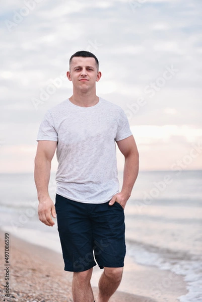 Obraz Young handsome smiling guy walks by the sea on the sand in summer