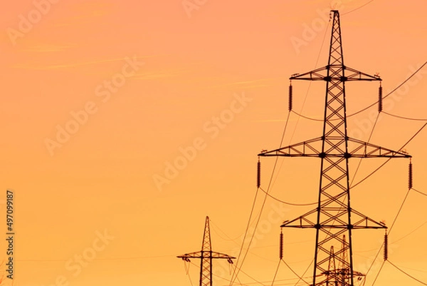 Fototapeta Background, view or scene of steel tower of electric main or electricity transmission line with the wires silhouette on yellow, orange and red background of sunset or sunrise sky