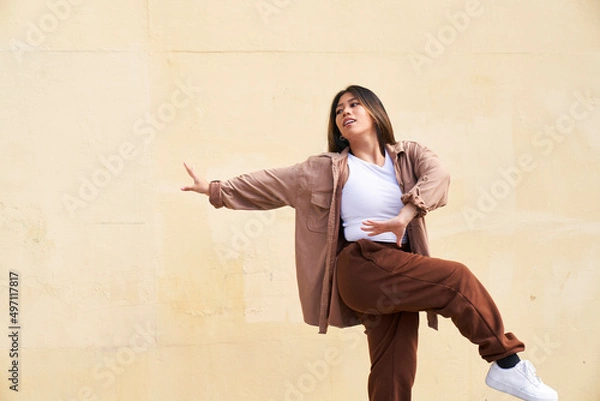 Obraz Woman dancing in front of beige wall kicking with arm extended