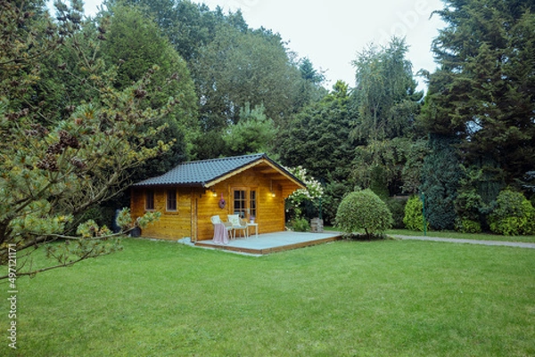 Fototapeta Modern garden chairs and flowers in front of a wooden hut. Garden joy in summer. Relax in the garden and enjoy the beautiful weather. Lavender and hydrangea in pot next to a garden shed