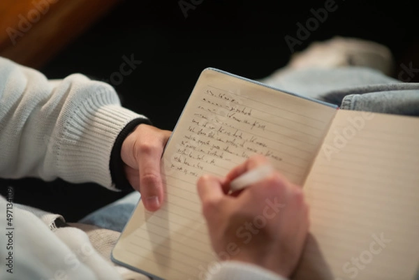 Fototapeta Close-up of young Caucasian man taking notes in notepad. Male student writing in notebook. Education concept
