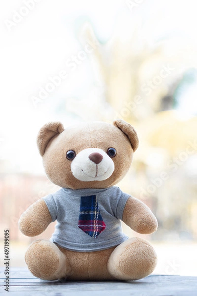 Fototapeta Vertical photo brown teddy bear in a shirt and tie sits on a wooden background with a green background background.