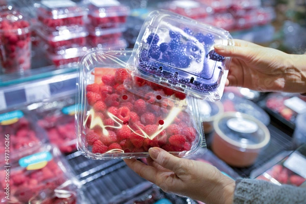 Fototapeta A woman's hand picks fresh berries and raspberries at the supermarket. Wide choice of fresh, organic and healthy products