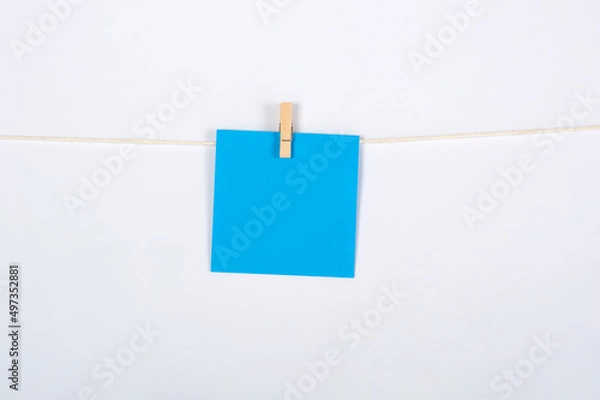 Fototapeta Post it azul colgado con pinza sobre fondo blanco para concepto ejercicio, recordatorio o mensaje.
