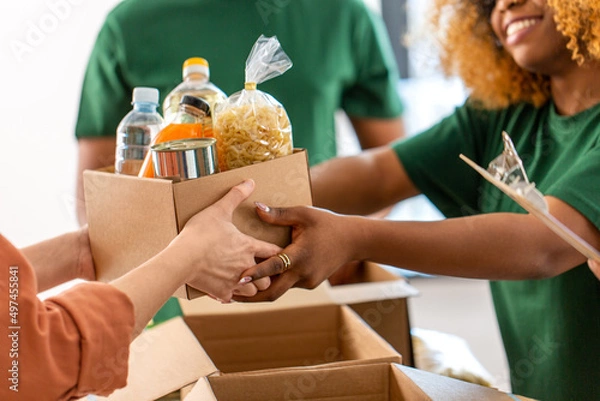 Fototapeta charity, donation and volunteering concept - close up of volunteers giving box of food at distribution or refugee assistance center