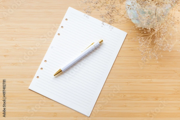 Fototapeta Flat lay, top view of blank, lined paper, flower bouquet and stationery on a wooden surface. Minimalistic workspace, creative writing, blogging, planning, business.
