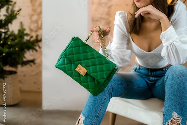 Fototapeta Stylish women's green handbag. Trendy outfit woman with green bag. Girl with bag over his shoulder outdoors. Shoulder Bags for Women. Fashion look woman outfit. Close-up.