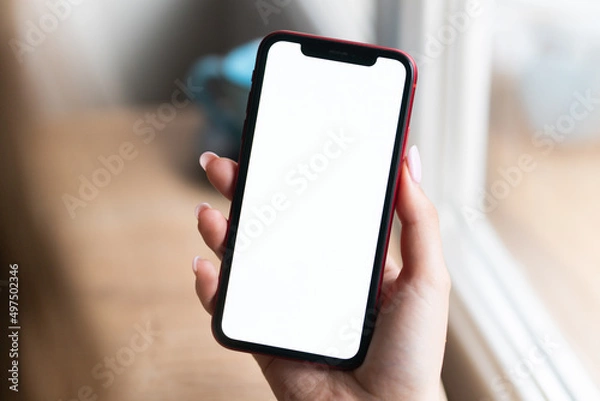 Fototapeta Young man hands holding mobile smart phone with mockup white blank display, empty screen at home. Shopping, delivery apps, social media applications ads,  close up view.
