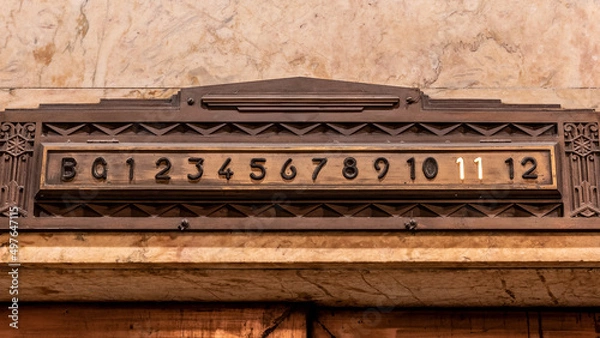 Fototapeta An Art Deco styled elevator floor indication made from brass set into a marble wall with the 11th floor Illuminated