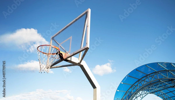 Fototapeta Side view of a basketball hoop with a backboard on a sports field, against a blue sky. Achievement, sports concept