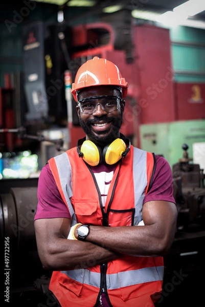 Obraz portrait of Happy african-american man worker have unkempt beard in safety uniform wearing helmet,glasses, vest and glove in industrial manufacturer factory.