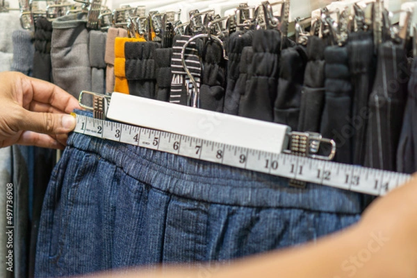 Fototapeta Woman's hand is measuring the waist of the pants with a tape measure in clothing store.