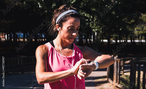 Fototapeta Young woman resting while looking at her results on a smartwatch after running. Healthy lifestyle. Selective focus.