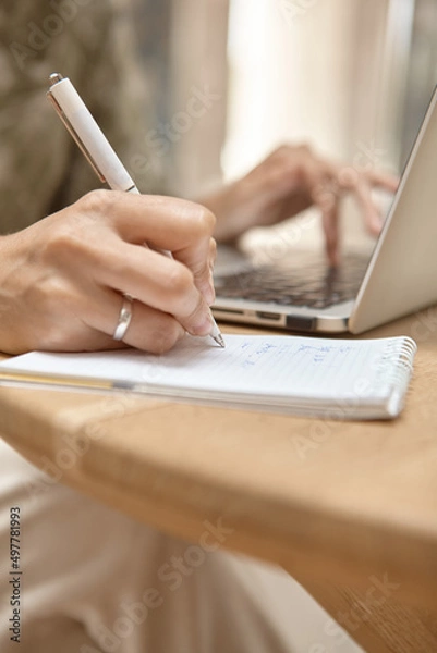 Fototapeta Close-up of a hand making a note. The laptop is running in the background. The concept of independent learning