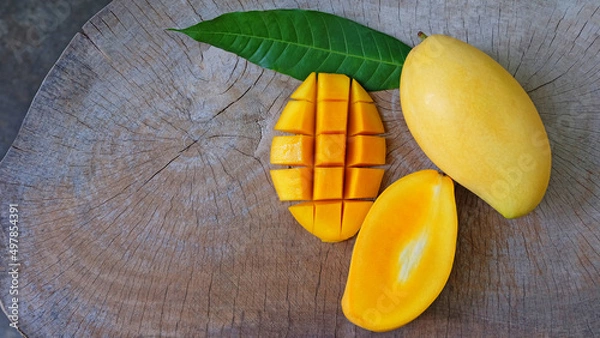 Obraz Mango fruit with mango cubes, cut in half and  green leaf on wooden table background.