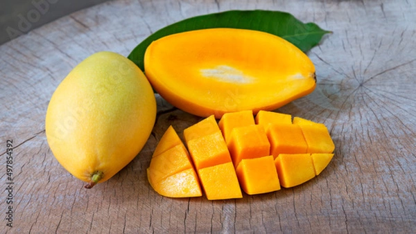 Obraz Mango fruit with mango cubes, cut in half and  green leaf on wooden table background.