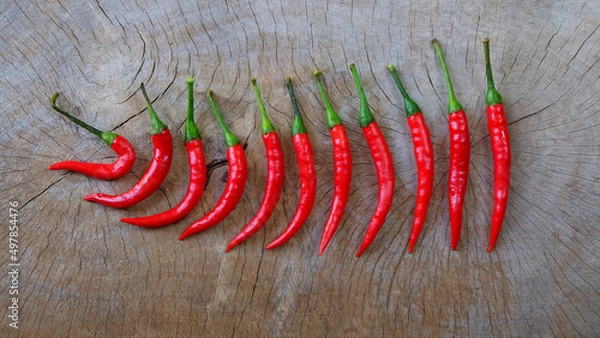 Obraz Red chili peppers arranged in a row on a wooden table background.