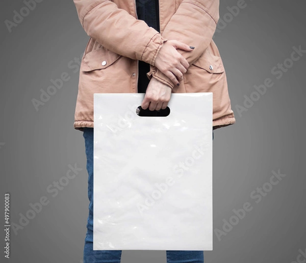 Fototapeta The girl is holding a mockup white plastic bag. A girl with a package on isolated background