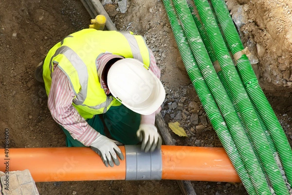 Obraz worker installing hdpe corrugated electric and sewer pipes at the construction site on street city