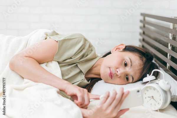 Fototapeta ベッドルームでスマホを見るミドル世代の女性
