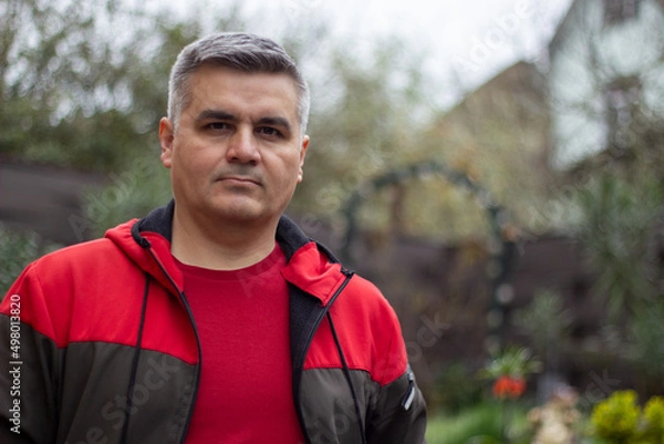 Fototapeta Portrait of a man 40-50 years old, gray-haired, swarthy. Serious look. Big eyebrows. Red jacket. Looking at the camera