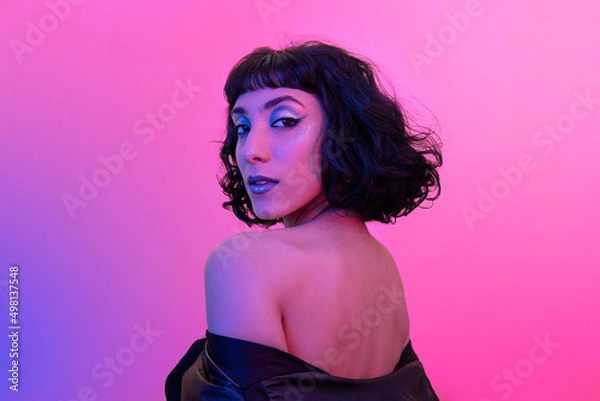 Fototapeta Young woman with bared back turns and looks into the camera. Portrait of smiling modern woman with trendy look and bright colors.
