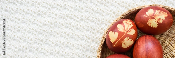 Obraz Panoramic photo. Top view of easter eggs, lying in wicker basket, on a lace tablecloth. Painted brown, with a plant theme. Easter concept.