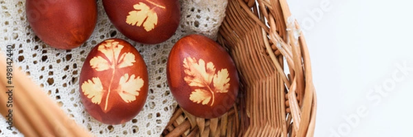 Obraz Panoramic photo. Top view od easter eggs, lying in wooden basket, on a lace doily. Painted brown, with a plant motif. Easter basket.