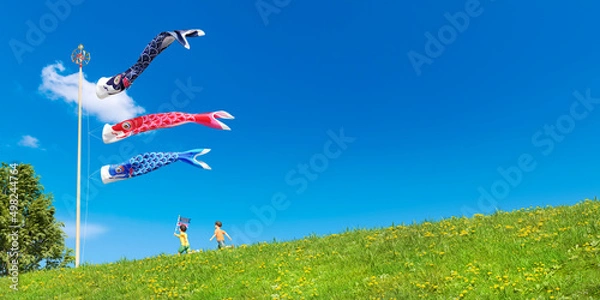 Obraz 鯉のぼりが気持ちよく泳ぐ土手沿いの道を走る元気な子ども / コピースペースのあるこどもの日・五月晴れ・端午の節句・爽やかな休日のコンセプトイメージ