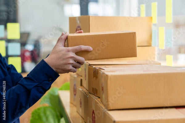 Fototapeta Small entrepreneurs start their SME business at home by arranging their products in yellow parcel boxes. The idea is to start selling online with laptops for taking orders and shipping.