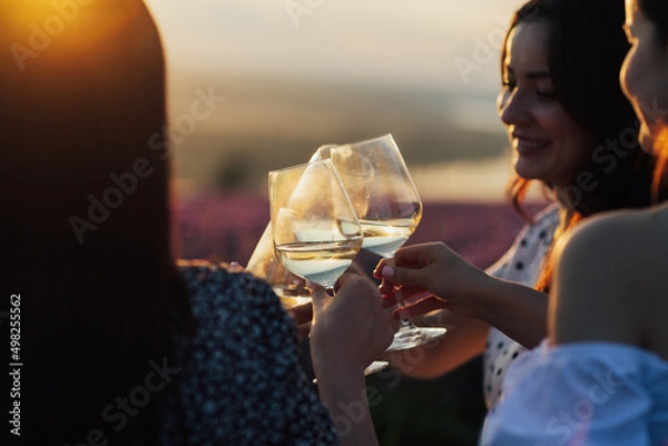 Fototapeta Close-up of hands holding glasses with white wine  during sunset. Celebration and friendship concept.