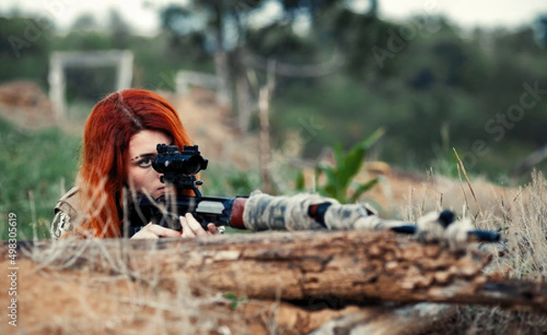 Fototapeta Sniper girl in a green field. Military snipers. The sniper smokes. Red-haired girl in camouflage. Fighting
