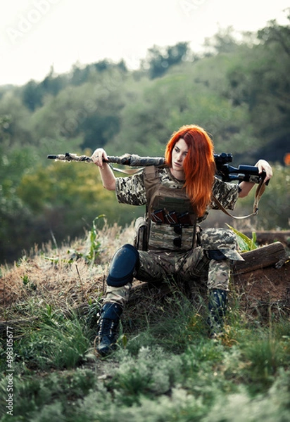 Fototapeta Sniper girl in a green field. Military snipers. The sniper smokes. Red-haired girl in camouflage. Fighting
