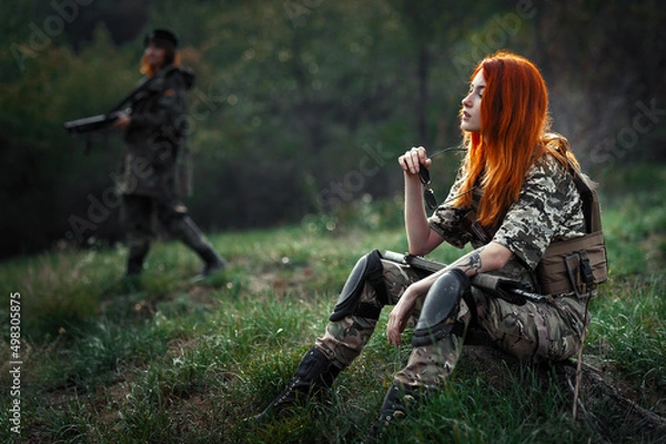 Fototapeta Sniper girl in a green field. Military snipers. The sniper smokes. Red-haired girl in camouflage. Fighting
