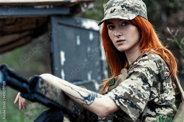 Fototapeta Sniper girl in a green field. Military snipers. The sniper smokes. Red-haired girl in camouflage. Fighting