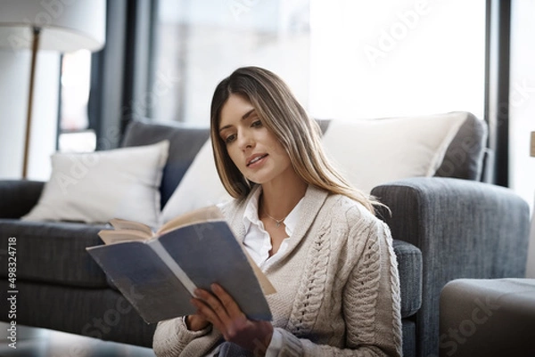 Fototapeta Nothing grabs my attention like a good read. Cropped shot of a beautiful young woman reading a book while relaxing at home.