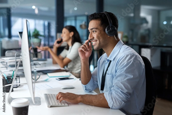 Fototapeta Dedicated service creates dedicated customers. Shot of a young man using a headset and computer in a modern office.