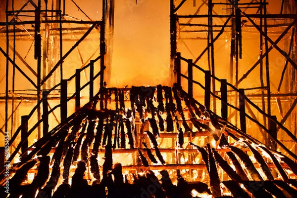 Fototapeta Burning bridge leading to the door of a destroyed burning building. Fiery bridge through the flames of fire. Burning collapsing wooden bridge in a raging flame close-up. Bridge on fire at dark night