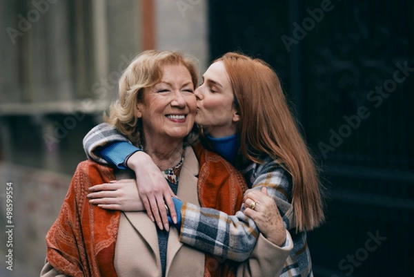 Obraz A happy grandmother and granddaughter hugging and kissing outside.