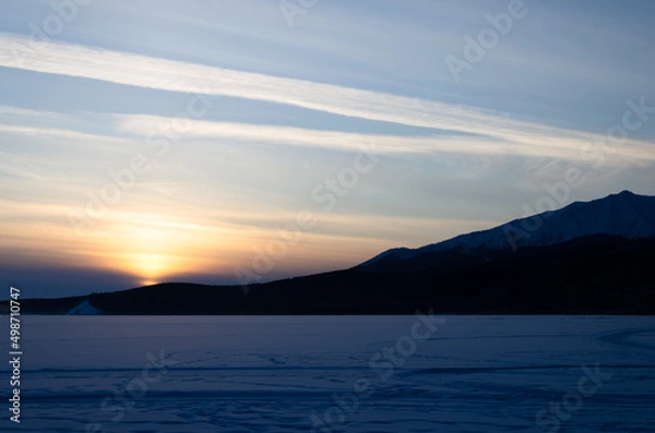 Fototapeta The last rays of the sun at sunset. The sun sets behind the mountains in the snowy desert.