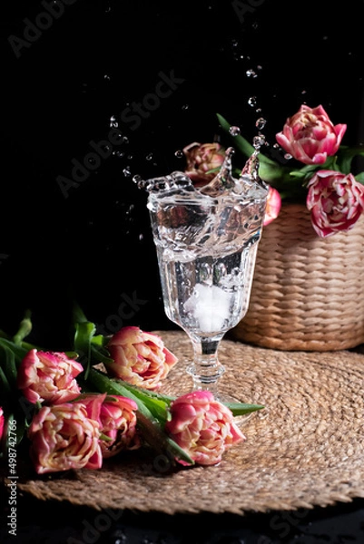 Fototapeta Splashing drink in the transparent glass with the pink tulips 