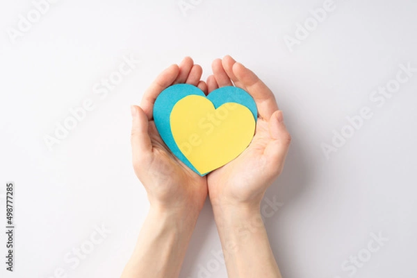 Fototapeta Stop the war in Ukraine concept. First person top view photo of girl's hands holding yellow and blue hearts on palms on isolated white background