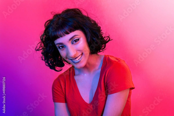 Fototapeta The young woman in the red t-shirt is looking at the camera. Portrait of smiling modern woman with trendy look and bright colors.