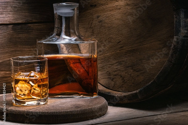 Obraz Bourbon whiskey is strong alcoholic beverage prepared by Irish monk. Grain whiskey from Scotland in wooden old barrel is poured whiskey into decanter and glass of ice of amber color.