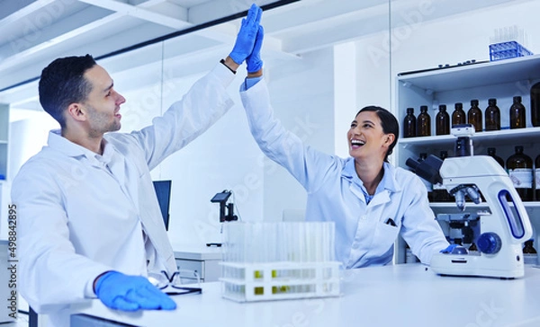 Fototapeta We did it. Cropped shot of two young scientists high fiving while working in their lab.