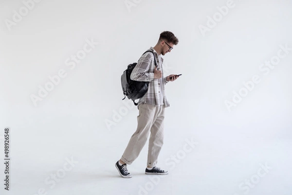 Obraz Side view portrait of a student walking with bag and mobile phone