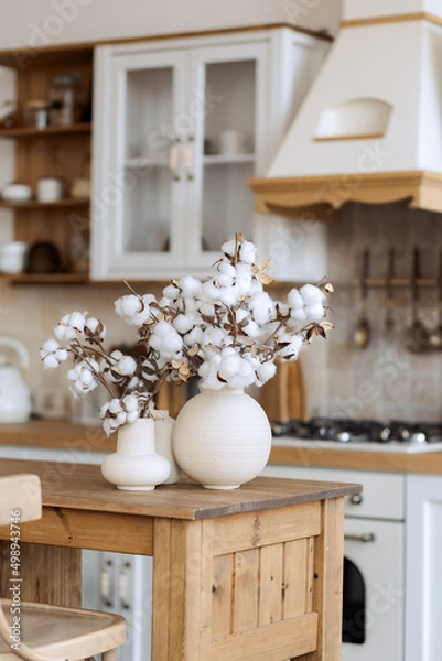 Obraz stylish kitchen in the old style, light, wooden, with stone tiles. Cotton in a vase. Composition in a ceramic pot.
